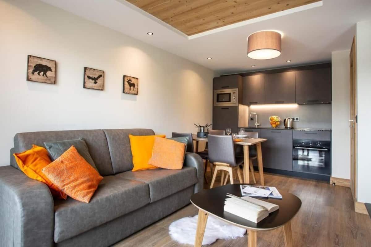 A modern living room with a grey sofa, wooden coffee table, and a dining area with a small table and chairs.