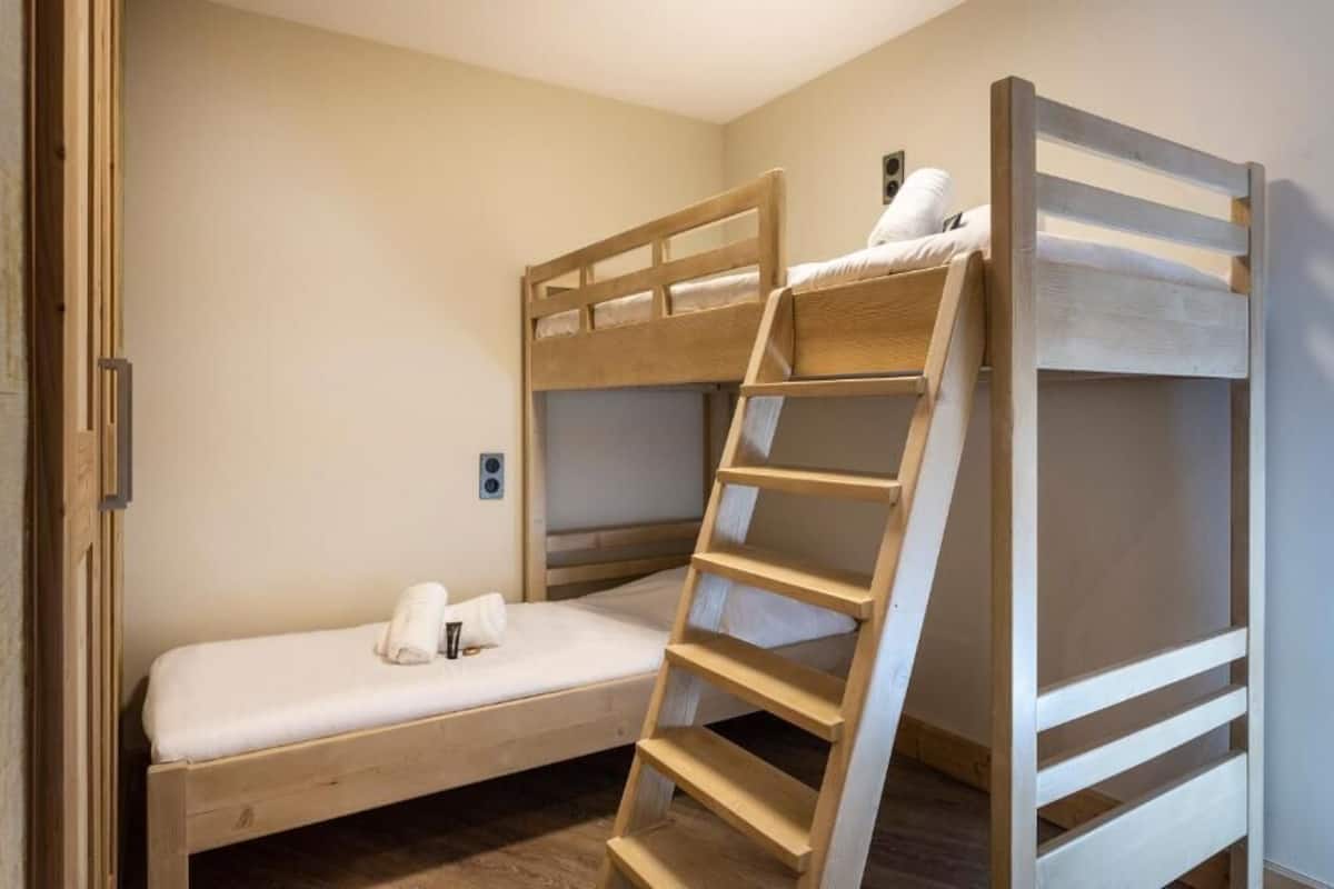 A bunk bed room with a wooden ladder, a small bedside table, and a wall-mounted light fixture.