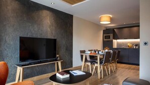 Una sala moderna con televisor de pantalla plana, un comedor con sillas, una cocina con armarios y una alfombra blanca y mullida.