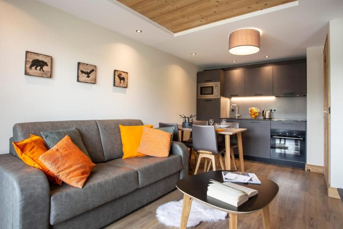 A modern living room with a grey sofa, wooden coffee table, and a dining area with a small table and chairs.