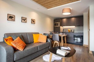 A modern living room with a grey sofa, wooden coffee table, and a dining area with a small table and chairs.
