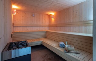 A sauna with wooden benches, a stone heating element, and a towel and wooden scoop on one bench.