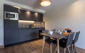 Una cocina moderna con armarios oscuros, un microondas integrado y un comedor con mesa y sillas de madera.