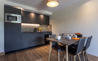 Una cocina moderna con armarios oscuros, un microondas integrado y un comedor con mesa y sillas de madera.
