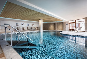 Ein Hallenbad mit Holzboden, gefliesten Wänden und Liegestühlen.