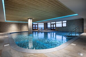 An indoor swimming pool with a wooden ceiling, stone walls, and a view of the sky.
