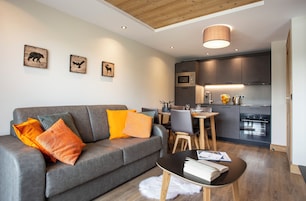 A modern living room with a grey sofa, orange pillows, a small round table, and a white furry rug.