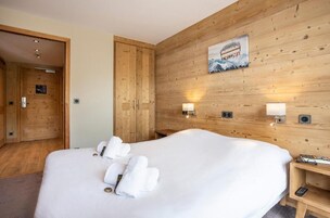 A hotel room with a wooden wall, a bed with white linens, and two wall-mounted lamps.