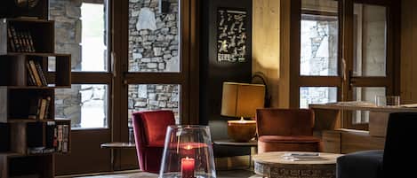 Une pièce chaleureuse avec un mur en pierre, un fauteuil rouge, une table en bois avec une bougie et une lampe.
