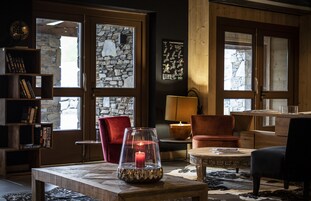 A cozy room with a stone wall, a red chair, a wooden table with a candle, and a lamp.