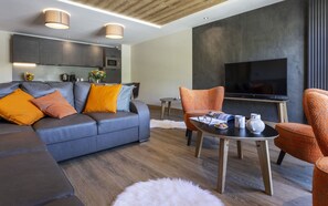 A modern living room with a grey sofa, orange cushions, a coffee table, and a flat-screen TV.