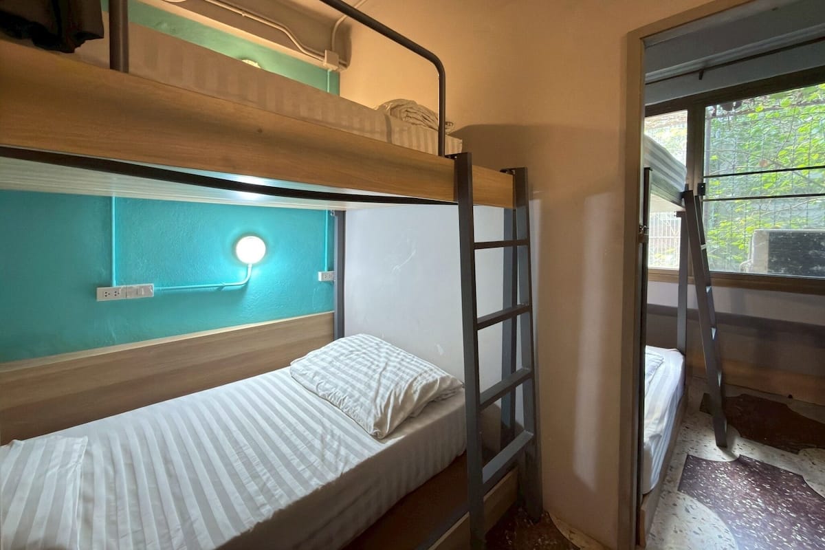 A bunk bed room with a ladder, a window, and a wall socket.