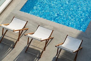 A poolside area with three wooden-framed lounge chairs and a clear blue pool. - Form Hotel Dubai (Dubai)