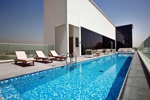 Et roolftop-infinity pool med liggestole, gelænder i glas og en moderne bygningsefacade.