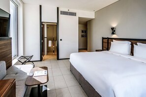 A hotel room with a bed, a small table, a sofa, a TV, and a door leading to another room. - Form Hotel Dubai (Dubai)