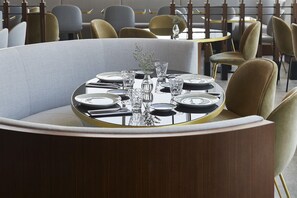 A round dining table with a glass top, surrounded by chairs with a light fabric upholstery. - Form Hotel Dubai (Dubai)