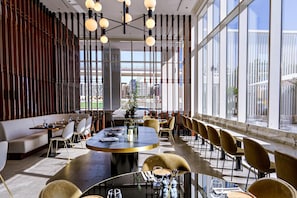 A modern restaurant with a long dining table, multiple chairs, and a large window offering a city view. - Form Hotel Dubai (Dubai)