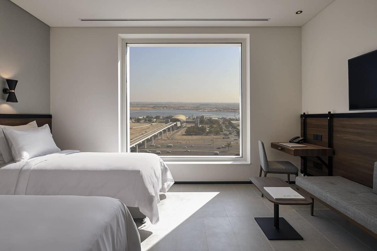 Ett modernt hotellrum med ett stort fönster, en säng, ett skrivbord och en stol.