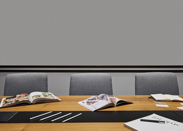 A conference room with a wooden table, three grey chairs, and various reading materials. - Form Hotel Dubai (Dubai)