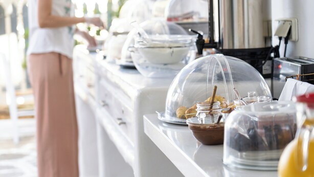 A buffet setup with covered food items and a person in the background. - Iris Boutique Hotel (Paros)