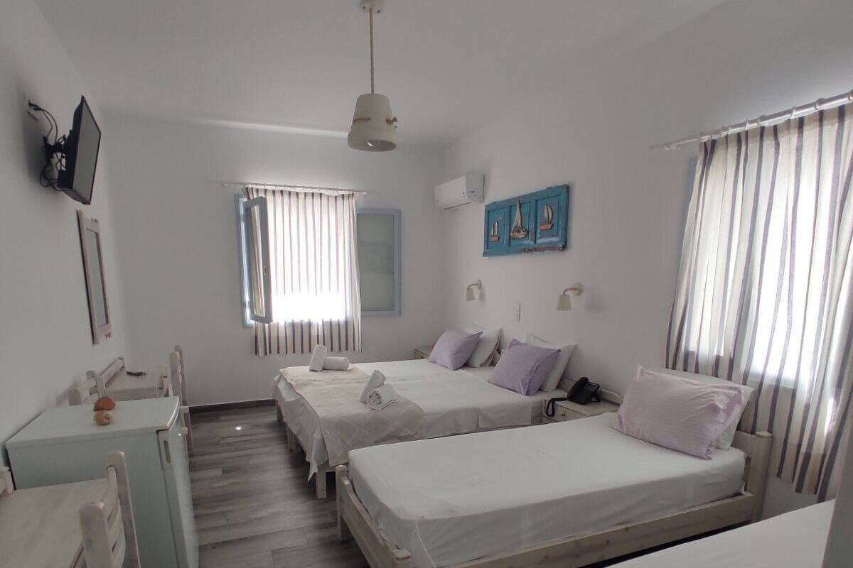A room with two beds, a desk, a chair, a window with curtains, a wall-mounted TV, and a ceiling fan.