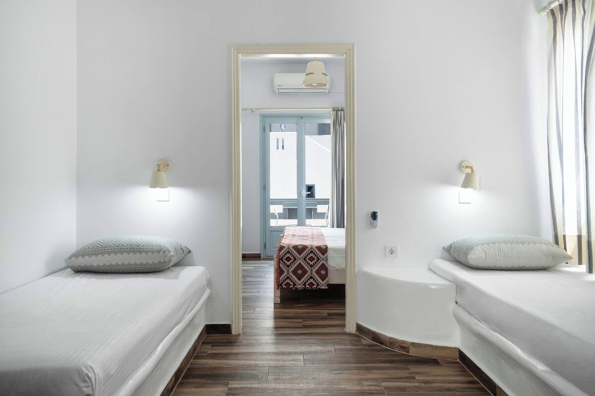 A room with two beds, a small table, and a door leading to an outdoor area.
