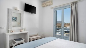 A bedroom with a bed, a desk, a chair, a TV, and a window with curtains. - Iris Boutique Hotel (Paros)