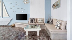 A living room with a beige sofa, a glass coffee table, and a wall-mounted TV. - Iris Boutique Hotel (Paros)