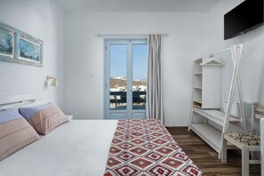 Quarto com cama, televisão, janela com cortinas e vista para edifícios.