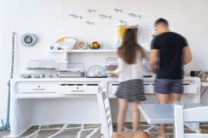 A kitchen area with white cabinets, a countertop, and a dining table. - Iris Boutique Hotel (Paros)