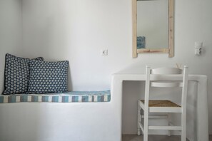 Una panca bianca con cuscini decorati, un piccolo ripiano bianco con un cesto intrecciato e uno specchio appeso al muro.