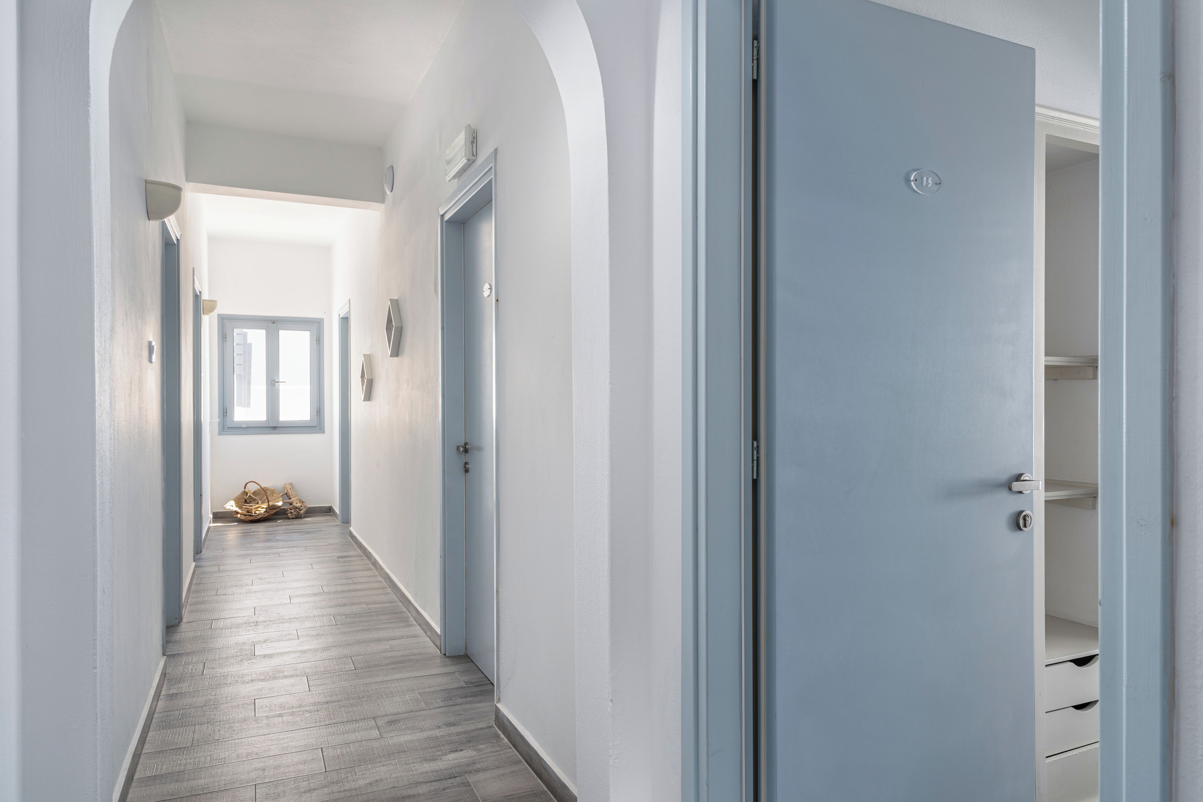Un pasillo con piso de madera, paredes blancas y una puerta azul.