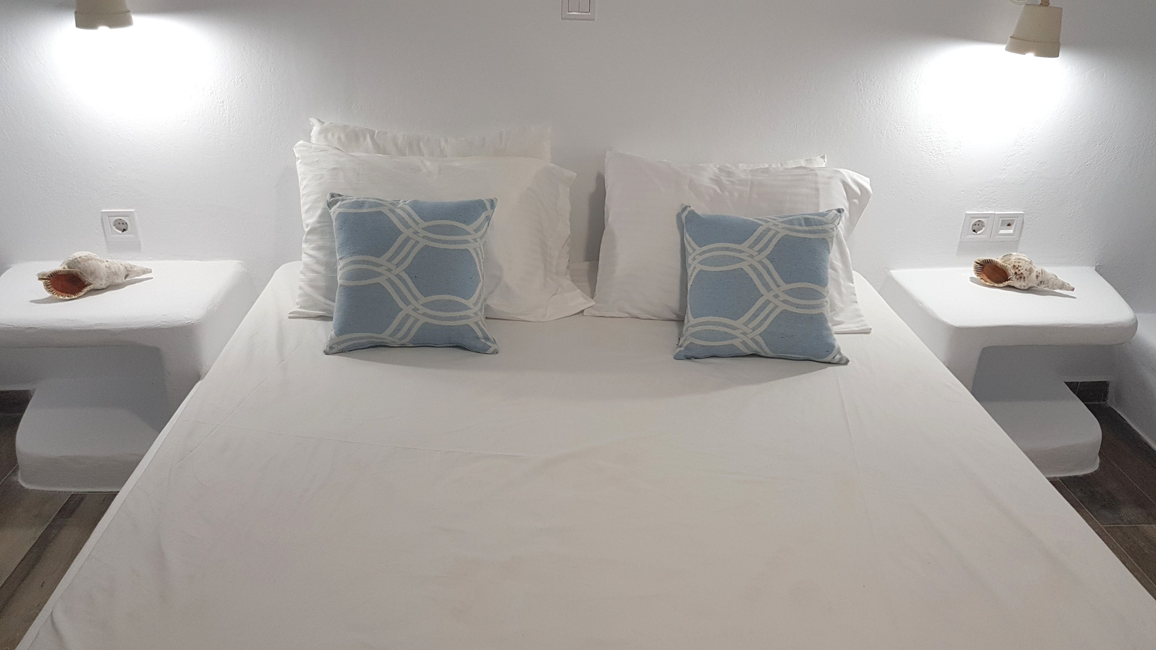 Habitación de hotel con una cama grande, dos mesitas de noche, ropa de cama blanca y conchas decorativas.