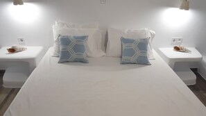 A hotel room with a large bed, two nightstands, white bedding, and decorative shells. - Iris Boutique Hotel (Paros)