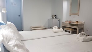 A hotel room with two beds, a desk, a small kitchenette, and a mirror on the wall.