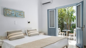 A bedroom with a bed, bedside tables, a wall-mounted air conditioner, and an open door leading to a balcony with chairs and a table. - Iris Boutique Hotel (Paros)
