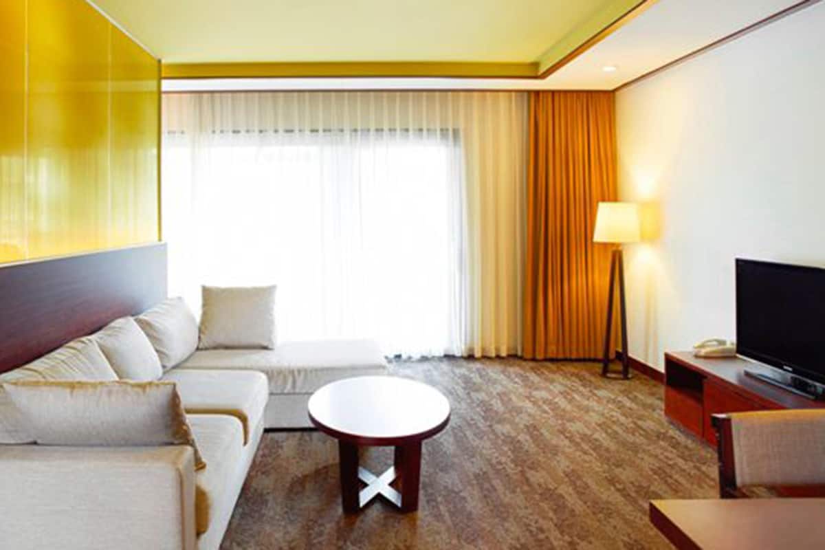 A hotel room with a sofa, a round coffee table, a TV, and a lamp.