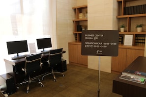 Un centro de negocios con dos estaciones de computadoras, un mostrador de recepción y una estantería con libros y objetos decorativos.