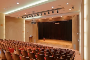 Un auditorio con filas de sillas, un escenario con un atril e iluminación empotrada en el techo.