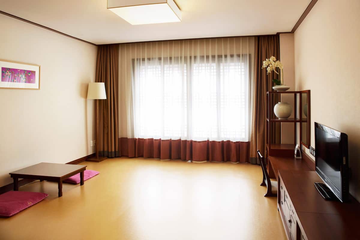 Habitación de hotel con un ventanal grande, un televisor de pantalla plana, un escritorio de madera y un estante pequeño con un florero.