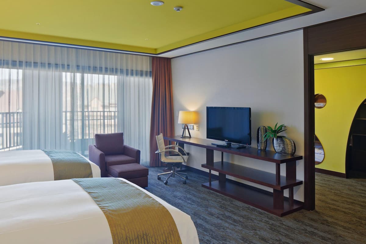 Habitación de hotel con dos camas, un escritorio con televisor, una silla y una lámpara de escritorio.