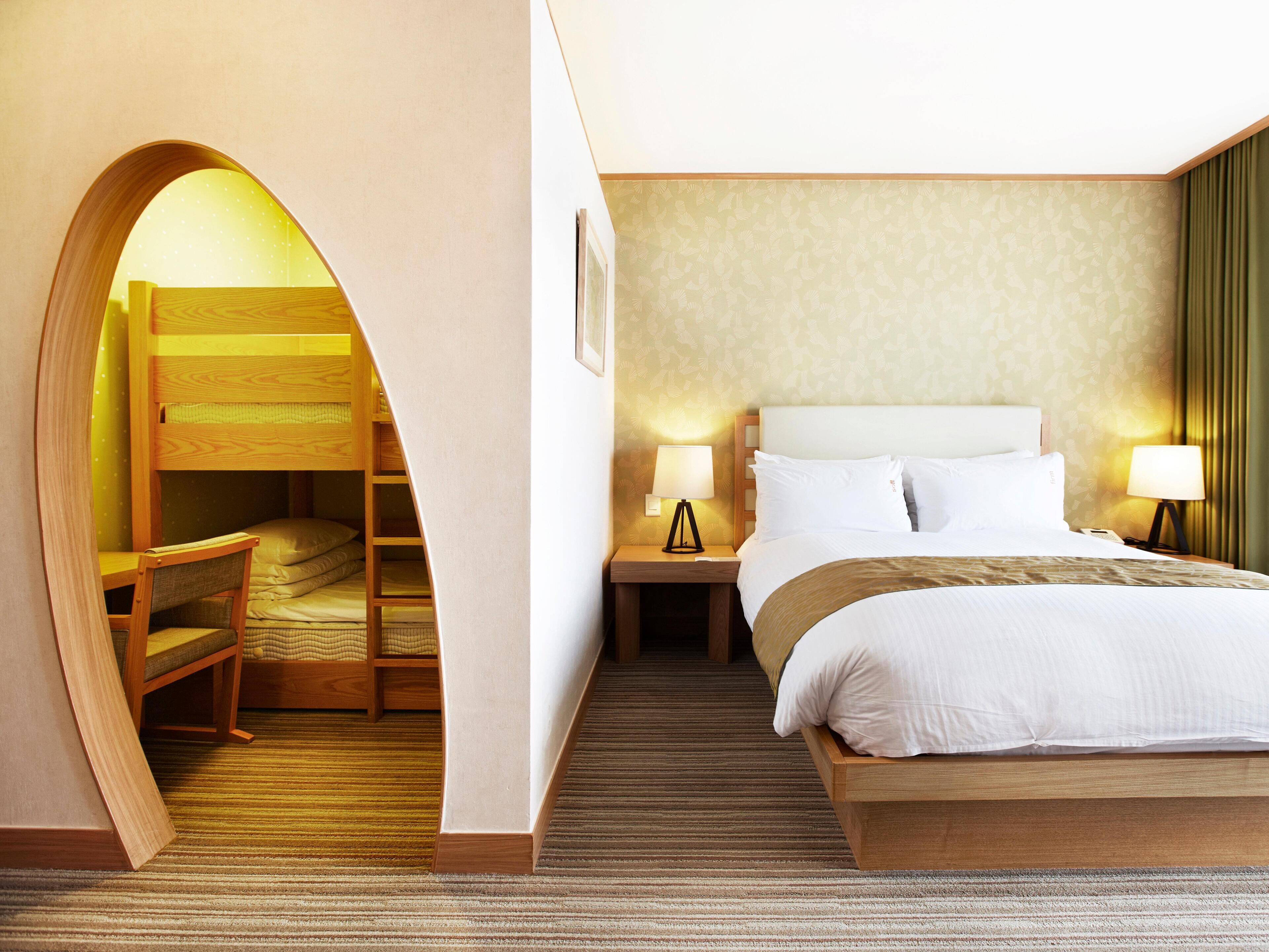 Una habitación de hotel con una cama nido, una cama individual, dos lámparas de noche, un cuadro en la pared y suelo alfombrado.
