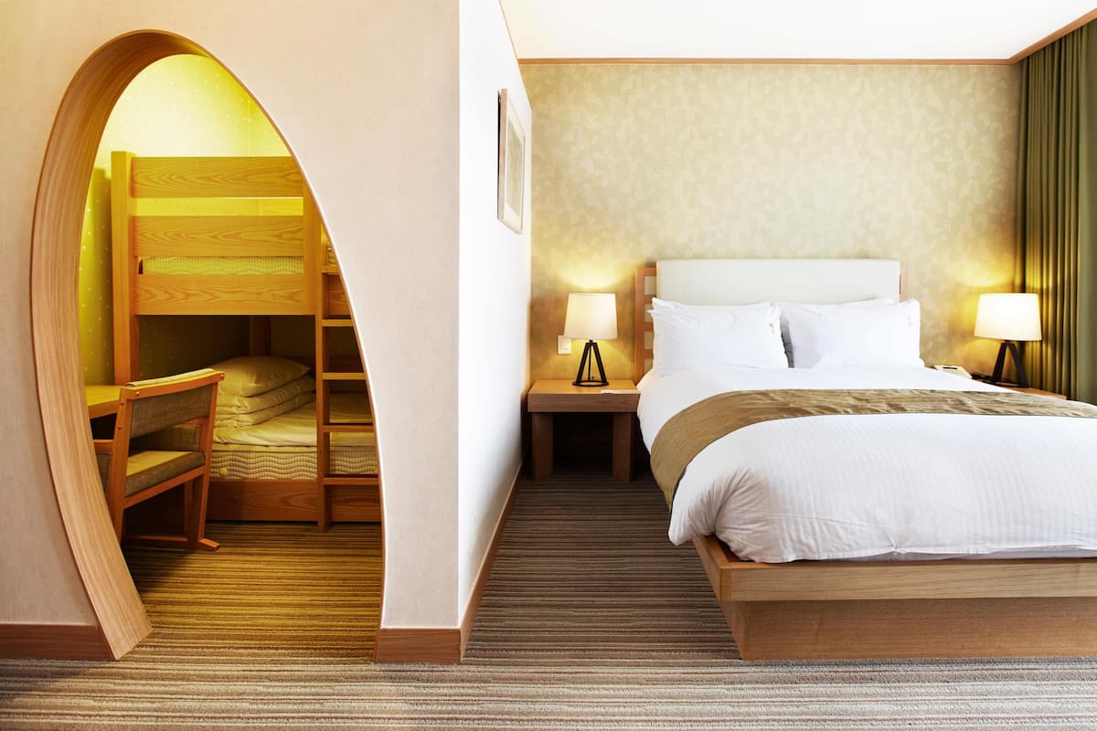 Una habitación de hotel con una cama nido, una cama individual, dos lámparas de noche, un cuadro en la pared y suelo alfombrado.
