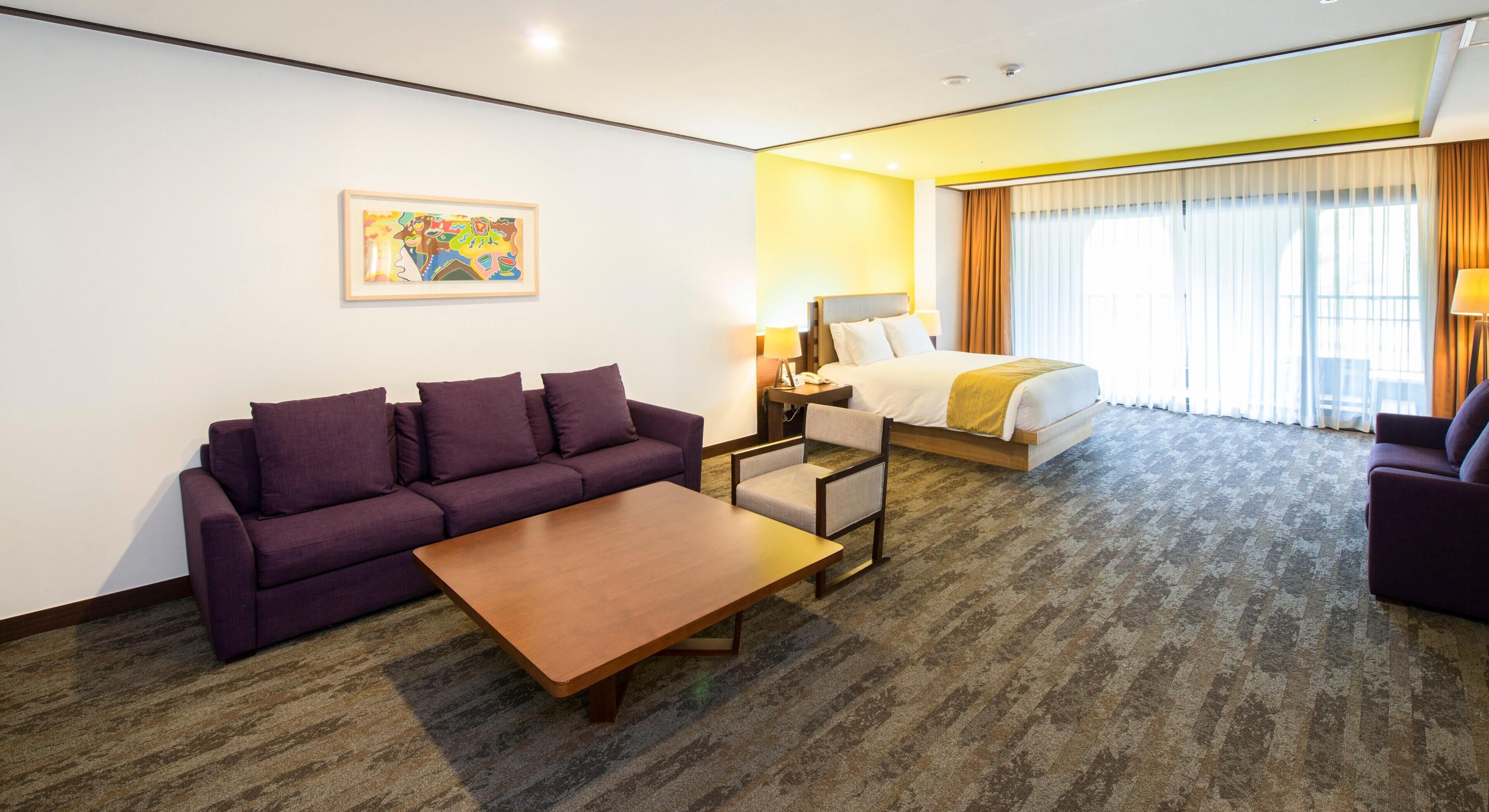 Una habitación de hotel con sofá, cama, escritorio y un cuadro en la pared.