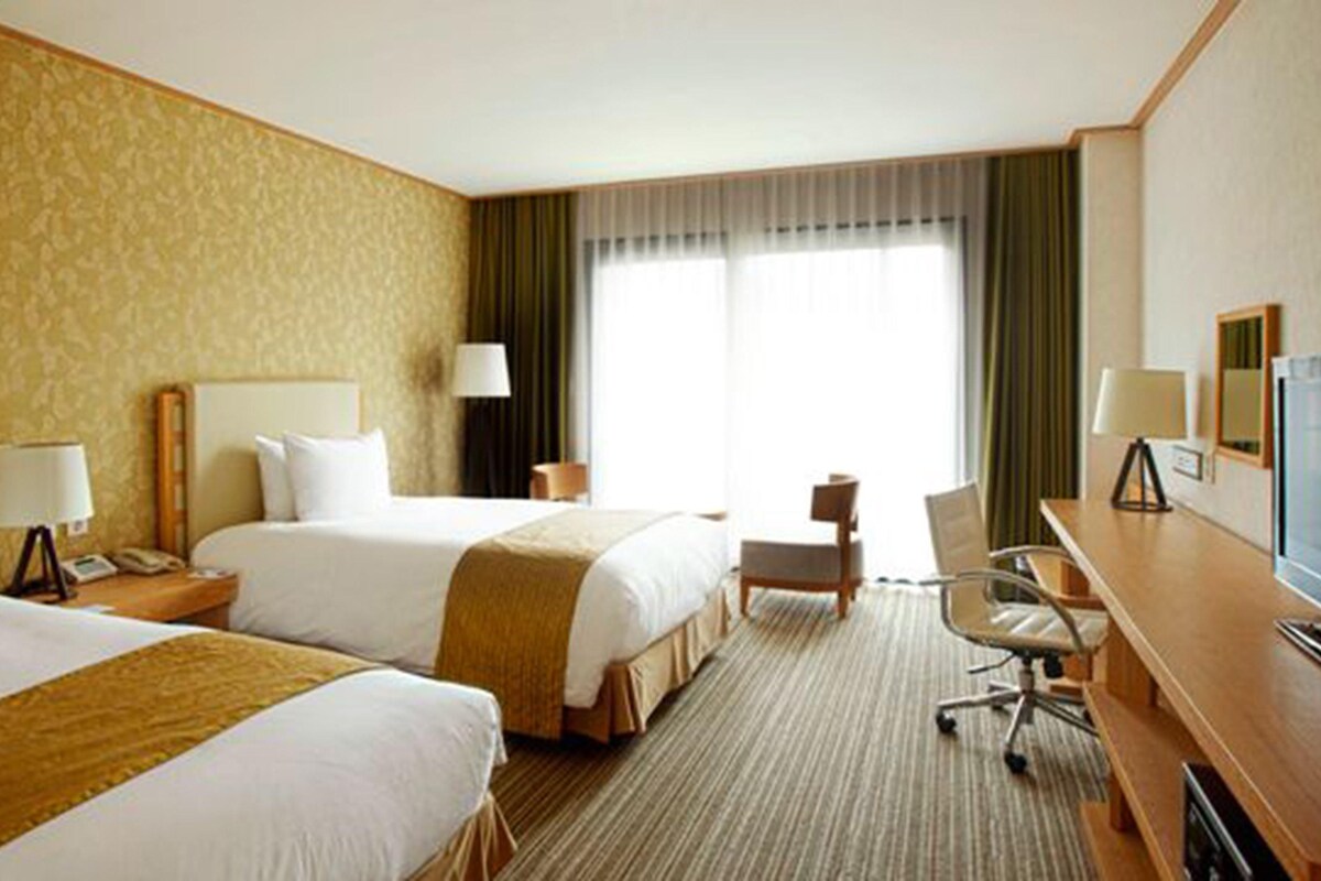 A hotel room with two beds, a desk, a chair, and a television.