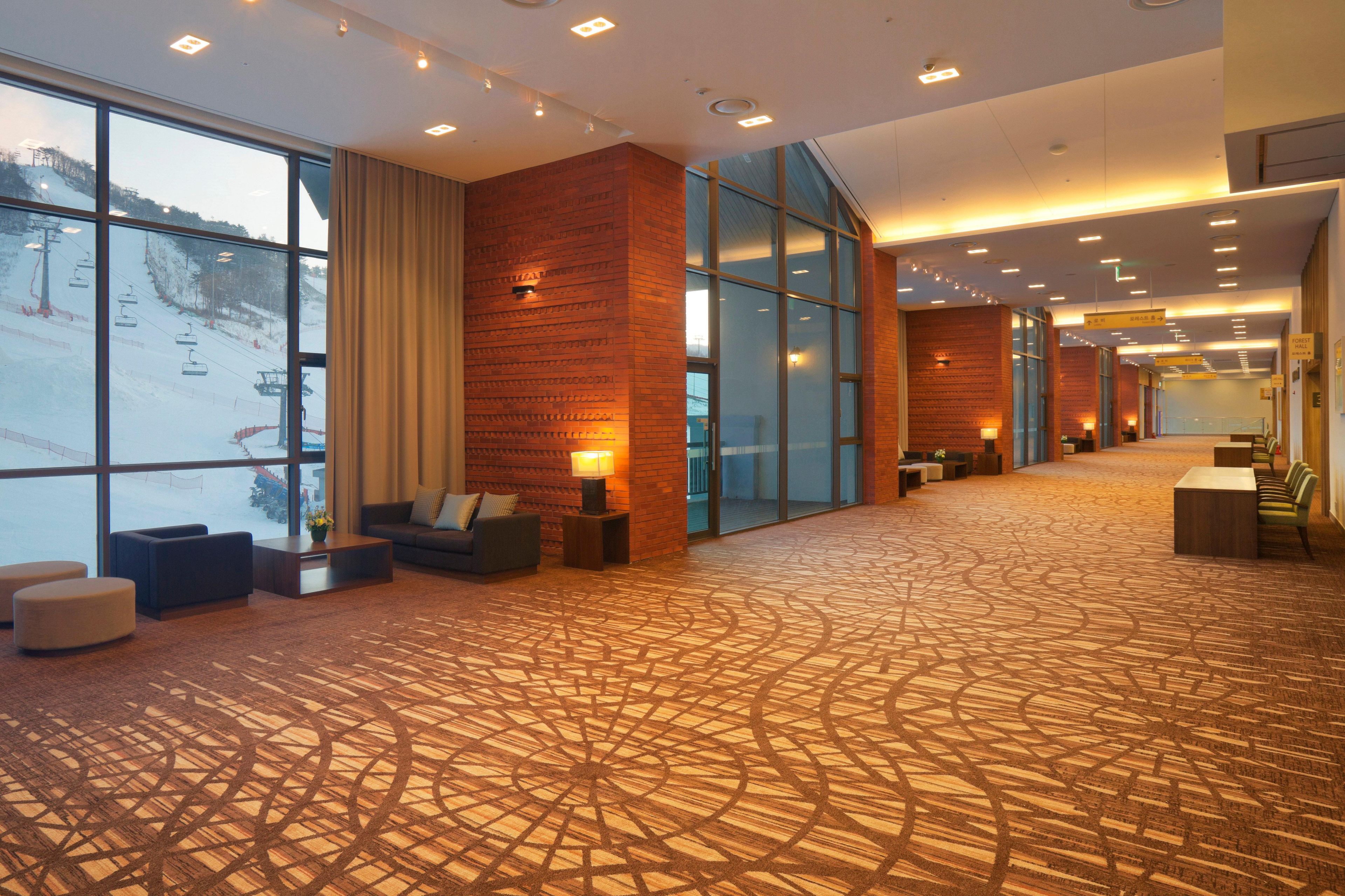 A spacious lobby with a patterned carpet, seating areas, and large windows offering a view of a ski slope.