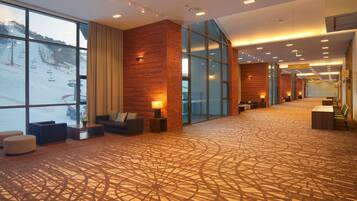A spacious lobby with a patterned carpet, seating areas, and large windows offering a view of a ski slope.