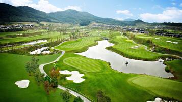A golf course with bunkers, water hazards, and a mountainous backdrop.