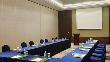A conference room with a long table, chairs, water bottles, and a projector screen.