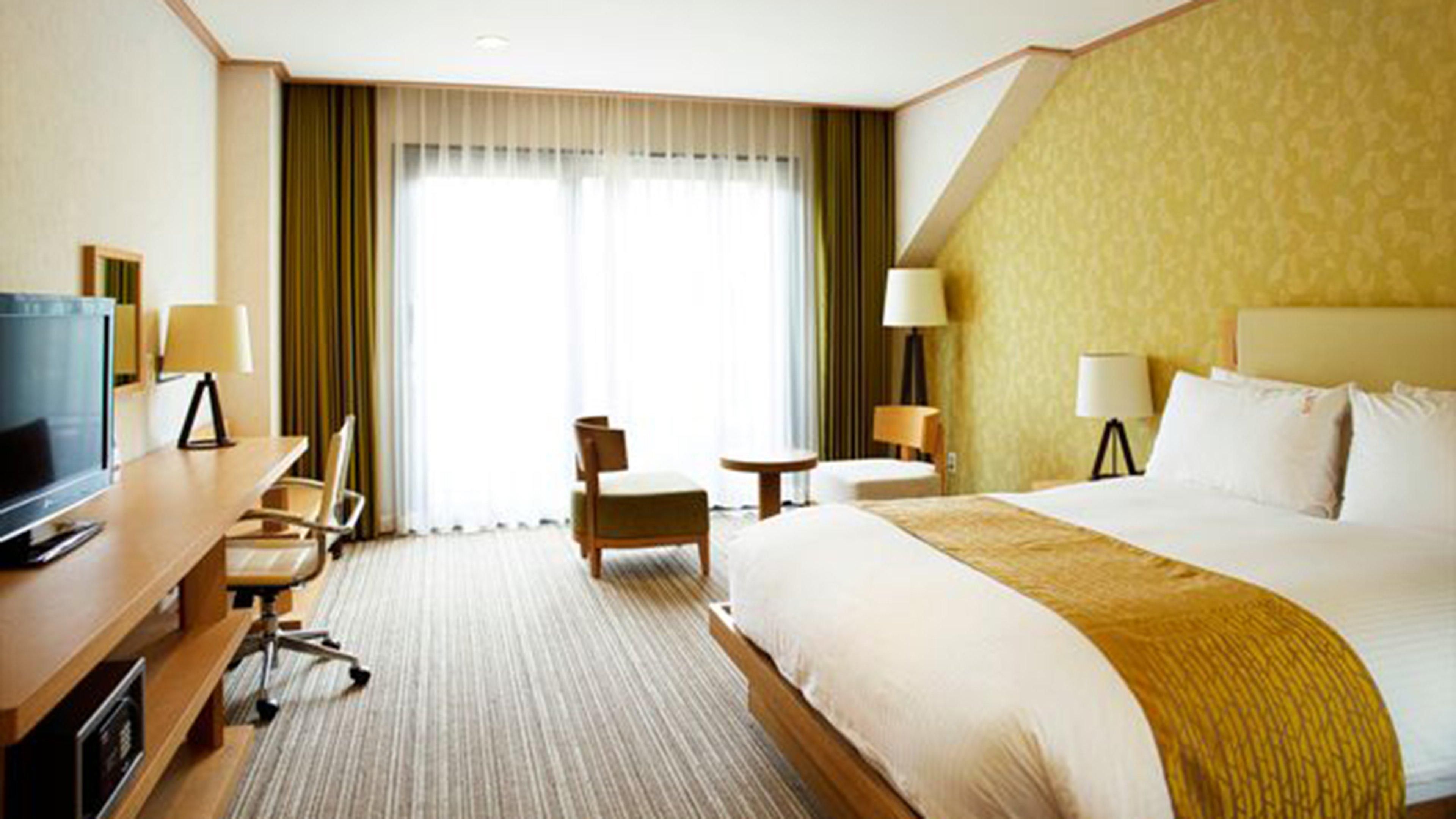 A hotel room with a large bed, a desk with a TV, a chair, and two lamps.